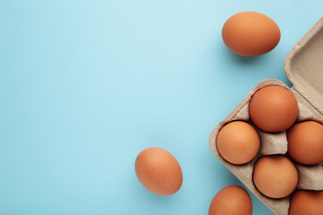 Chicken eggs in an open egg carton on blue. Top view with copy space. Natural healthy food and...