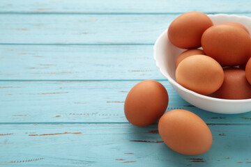Top view of raw brown eggs on plate on blue wooden background. Eggs are a common ingredient in cooking.