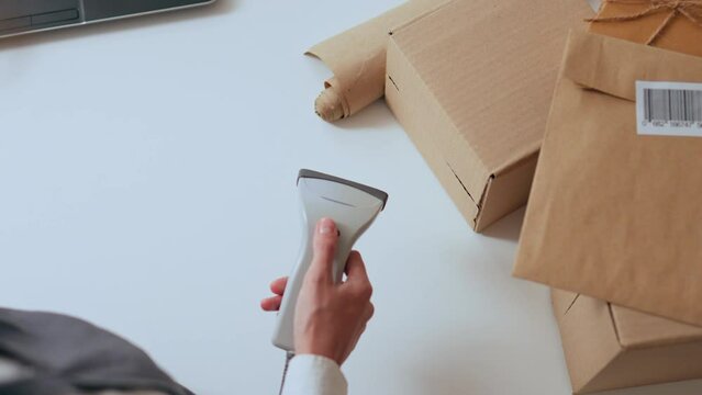 A woman worker scans postal envelopes, entering information about the parcel into the database, the process of scanning the barcode printed on the parcel to be sent by the transport company
