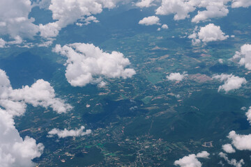 Aerial view from the top view of the forest, mountain, meadow and abundant plantation fields, covered by white fluffy clouds