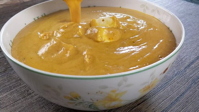 Home made paneer butter masala transferring to a bowl.  Paneer butter masala made with home made fresh paneer and other ingredients.
