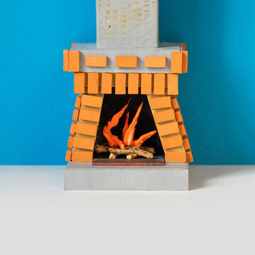 Toy fireplace interior. Chimney decorated with bricks. Firewood with flame lights inside the mantle. Blue gray background