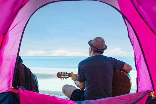 Young man on the beach playing &nbsp;parlo&nbsp;acoustic guitar while sporting a purple tie-dye t-shirt.