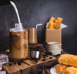 Pour milk to make iced latte coffee into the glass with 
dessert, roasted coffee beans on a black background 