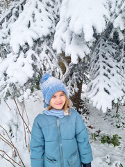 a cute girl in a blue coat under a snow-covered spruce. the beauty of winter nature, winter games and entertainment with children.