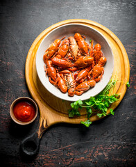 Boiled crayfish in a bowl on a cutting Board with parsley and sauce.