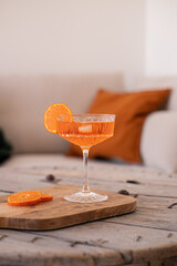 Home minimal concept. Sok drink pomarańczowy w salonie w domu. Sok drink w kieliszku na nodze, beżowe tło, minimalizm. Orange drink aperol in glass, beige background. 