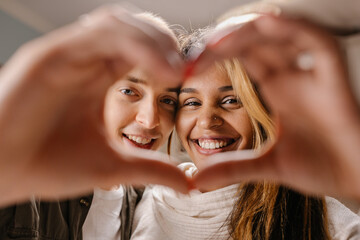 White guy and Black girl couple at home making heart sign with hands, smiling and looking at camera.