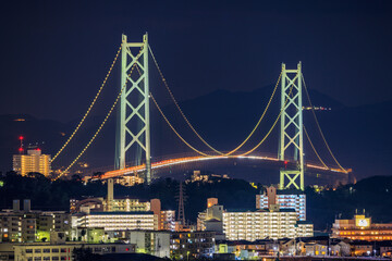 Obraz premium Illuminated Suspension Bridge Towers Over Apartment Buildings at Night