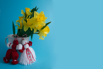 Bouquet of yellow daffodils tied with red-white martenitsa, martisor on blue background 