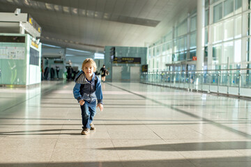 Fototapeta na wymiar Cute baby boy waiting boarding to flight in airport transit hall near departure gate. Active family lifestyle travel by air with children