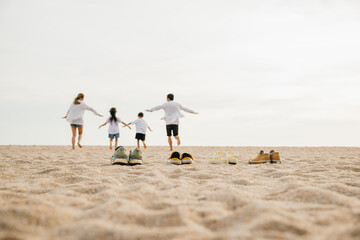 Happy family day. lifestyle father, mother and kids take off shoes running on sand, Back view Asian...