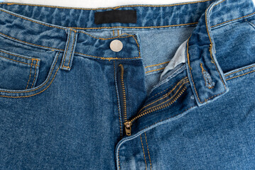 Unbuttoned blue jeans or shorts with empty black label. Part of denim clothes close-up