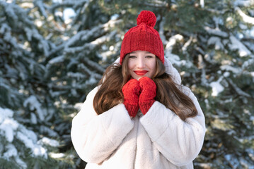 Portrait of happy young girl in knitted red hat and mittens on snowy trees background. Little red riding hood