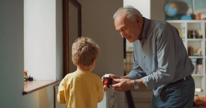 Portrait of a Senior Man at Home Giving his Grandson a Truck so he can Play with it. Caring and Affectionate Grandfather Looking after a Little Cute Boy and Giving him a Gift