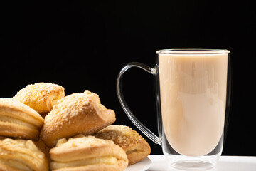 Tea with milk in a glass cup with a double bottom and cakes on a black background