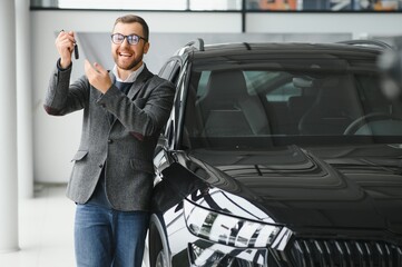 Happy owner of a new car. Emotional handsome man in casual clothes is happy, buying a car in the dealership.