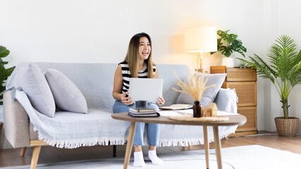 Fototapeta premium Woman using laptop to work or do homework at home with smiling face in her living room, Creating happiness at work with a smile, Live performance or video call with laptop, Work from home.