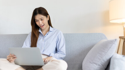 Fototapeta premium Woman using laptop to work or do homework at home with smiling face in her living room, Creating happiness at work with a smile, Live performance or video call with laptop, Work from home.