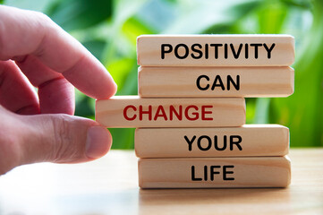 Positivity can change your life text on wooden blocks with hand and blurred nature background. Motivational concept