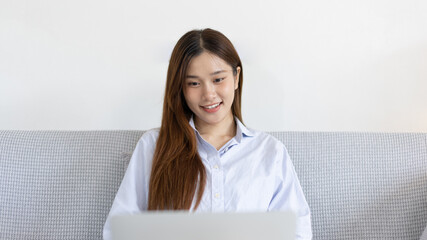 Woman using laptop to work or do homework at home with smiling face in her living room, Creating happiness at work with a smile, Live performance or video call with laptop, Work from home.