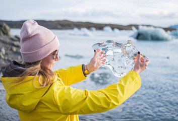 Blond Woman in Yellow Coat Walking on Glacial Lagoon in Iceland, Atlantic Ocean, Sunny Day