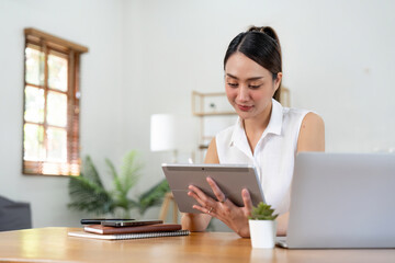 Portrait of young asian woman holding stylus pen while working on tablet computer at home