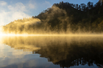 Peaceful misty morning at the Ranu Kumbolo in the Mt. Semeru National Park in Indonesia with Autumn colours reflecting in still calm water.