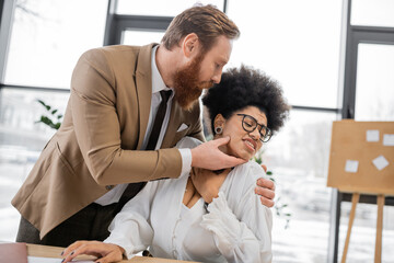 bearded businessman seducing scared african american woman in office.