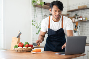 Obraz na płótnie Canvas Happy asian man preparing vegetable salad in kitchen.