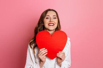 portrait of a woman holding big red heart card isolated on pink background