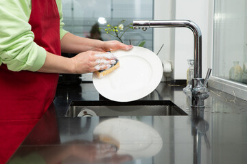 a girl in a red apron washing dishes in the kitchen