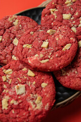 Delicious cookies with white chocolate chips in a dark plate on a red background. You can see the texture of the cookies