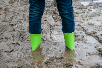 Rubber boots stuck in mud. Dirty rubber boots of green color on a dirt road. Dirty waterproof shoes, autumn concept.
