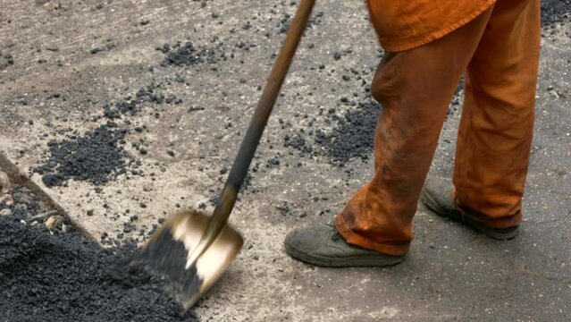Construction workers in uniform level the loose fresh asphalt with shovels and other construction tools.

Unmodified camera color.