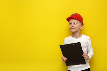 boy in a construction safety helmet with a tablet in his hands looks up on a yellow background with copy space