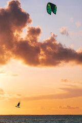 Sunset sky over the Indian Ocean bay with kiteboarder jumping trick on kiteboard with a green bright power kite. Active sport people and beauty in Nature concept image. Le Morne beach, Mauritius.