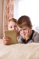 Children are lying on the bed, watching cartoons, playing a game on smartphone