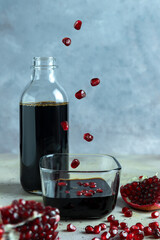 Natural organic pomegranate sause in glass cup and bottle. Cut pomegranate fruit and flying grains...