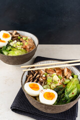 Bowls of ramen soup with chicken breast, vegetables, mushrooms and egg on a gray napkin on a white wooden table and chopsticks. Top front view, healthy eating concept