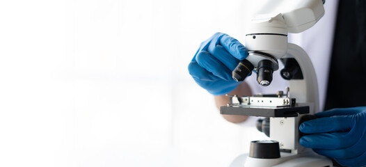 Biological scientist looking at samples by using microscope doing research for new vaccine in pharmaceutical laboratory.