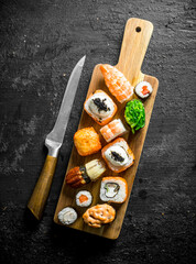 Sushi rolls with shrimp, vegetables and salmon on a cutting Board with a knife.