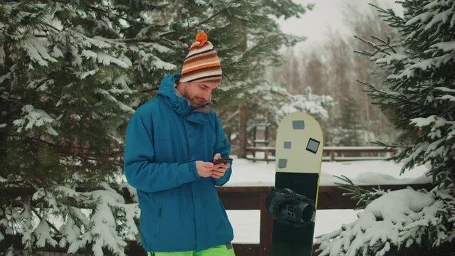 Snowboarder man rider in the snow at ski resort, using his smart phone while resting in the mountains, sport application, navigation and booking, communication, sport lifestyle