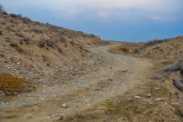 Curved dirty ascending road covered by rocks in a treeless steppe © Vardan