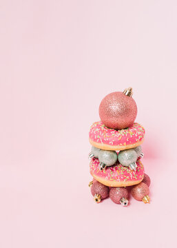 Donut tower made of pink donut and Christmas baubles on bright pink background. Creative idea of Christmas tree with sugar taste. Minimal donut cake concept.