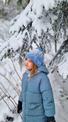a cute girl in a blue coat under a snow-covered spruce. the beauty of winter nature, winter games and entertainment with children.