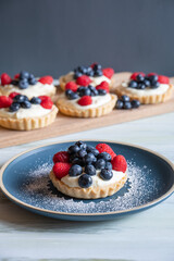A selection of blueberry and raspberry tarts on a white table in front of a grey background.