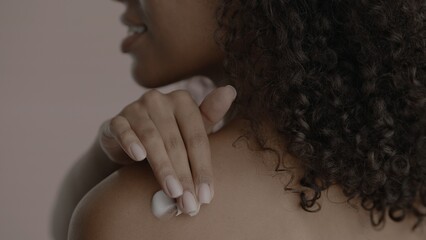 CU Back view, African-American female rubbing cream onto her shoulder. Studio shot, soft lighting....
