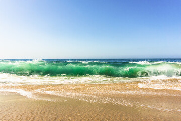 Low angle view of turquoise waves crashing onto  beach with blue sky above