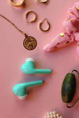 Face massager, various accessories, jewelry and wireless headphones on pink background. Top view.